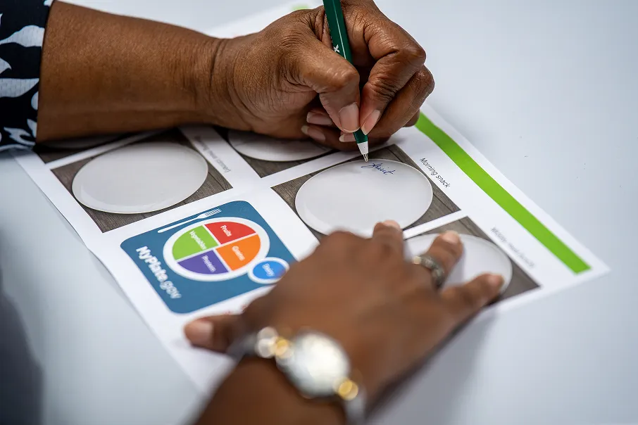 Person writing on a food planning sheet labeled 'MyPlate.gov' showing meal sections with a pen.