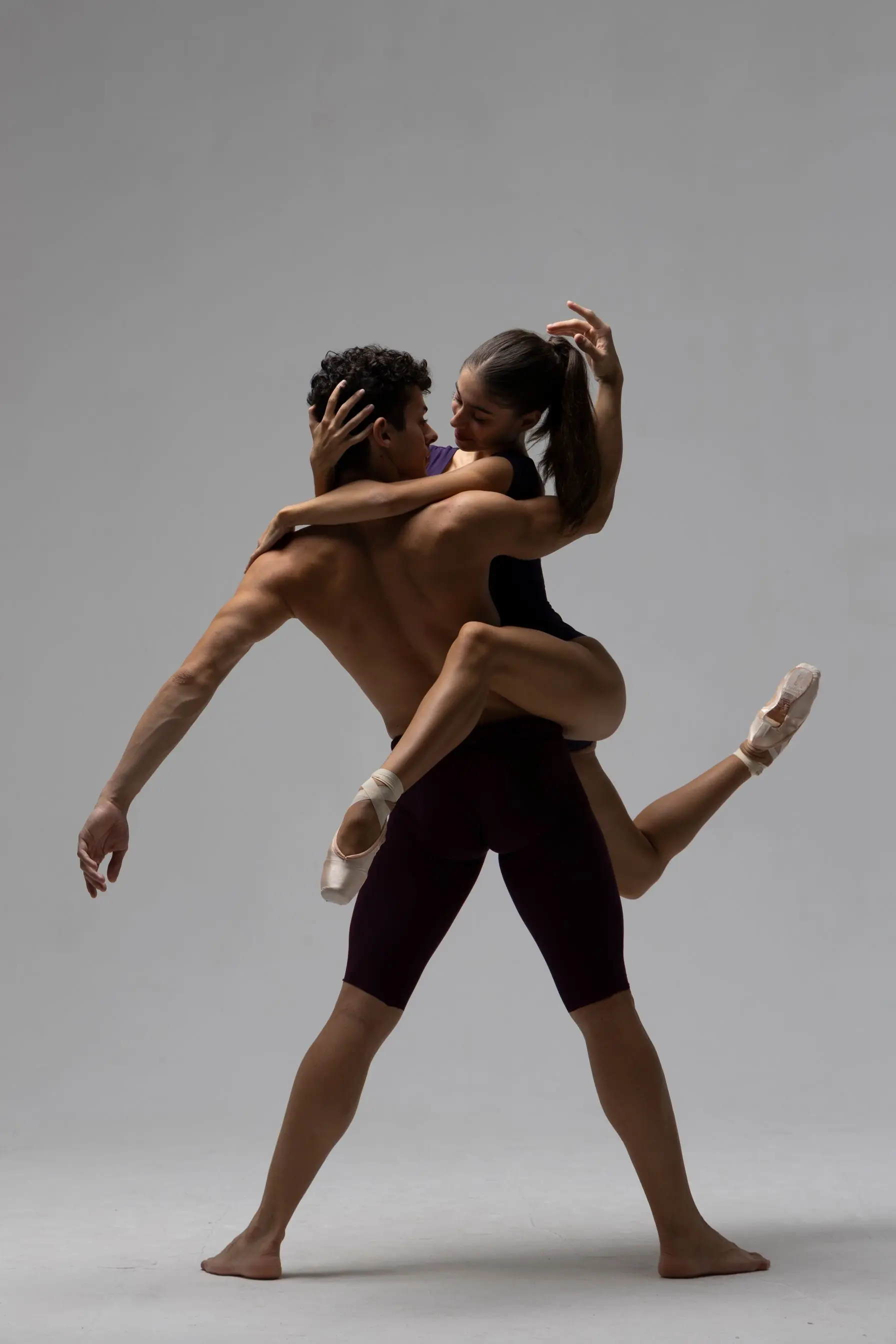 Male dancer lifting and holding female ballerina midair against a plain gray background.