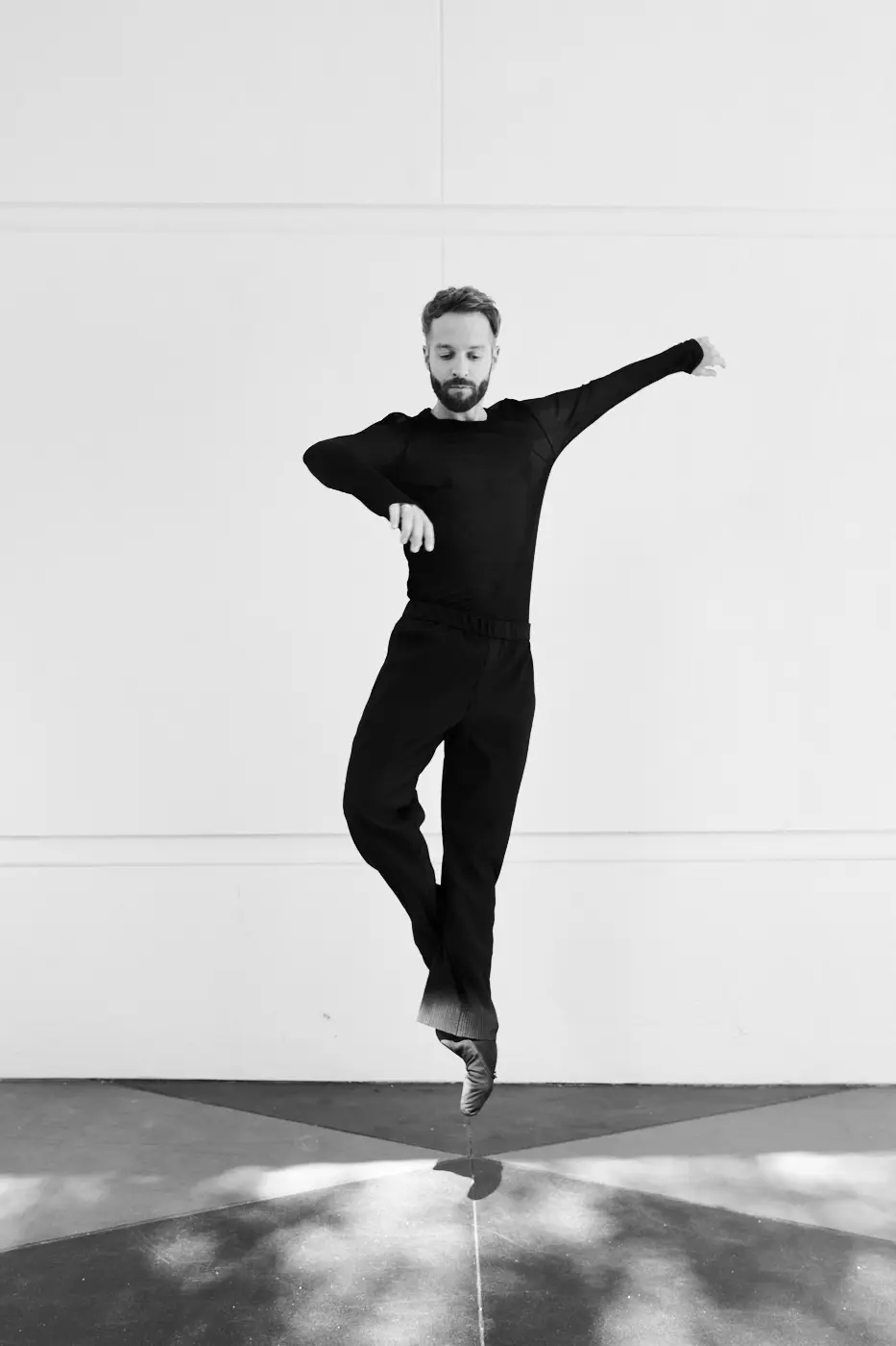 Man in black striking a graceful pose against a white background.