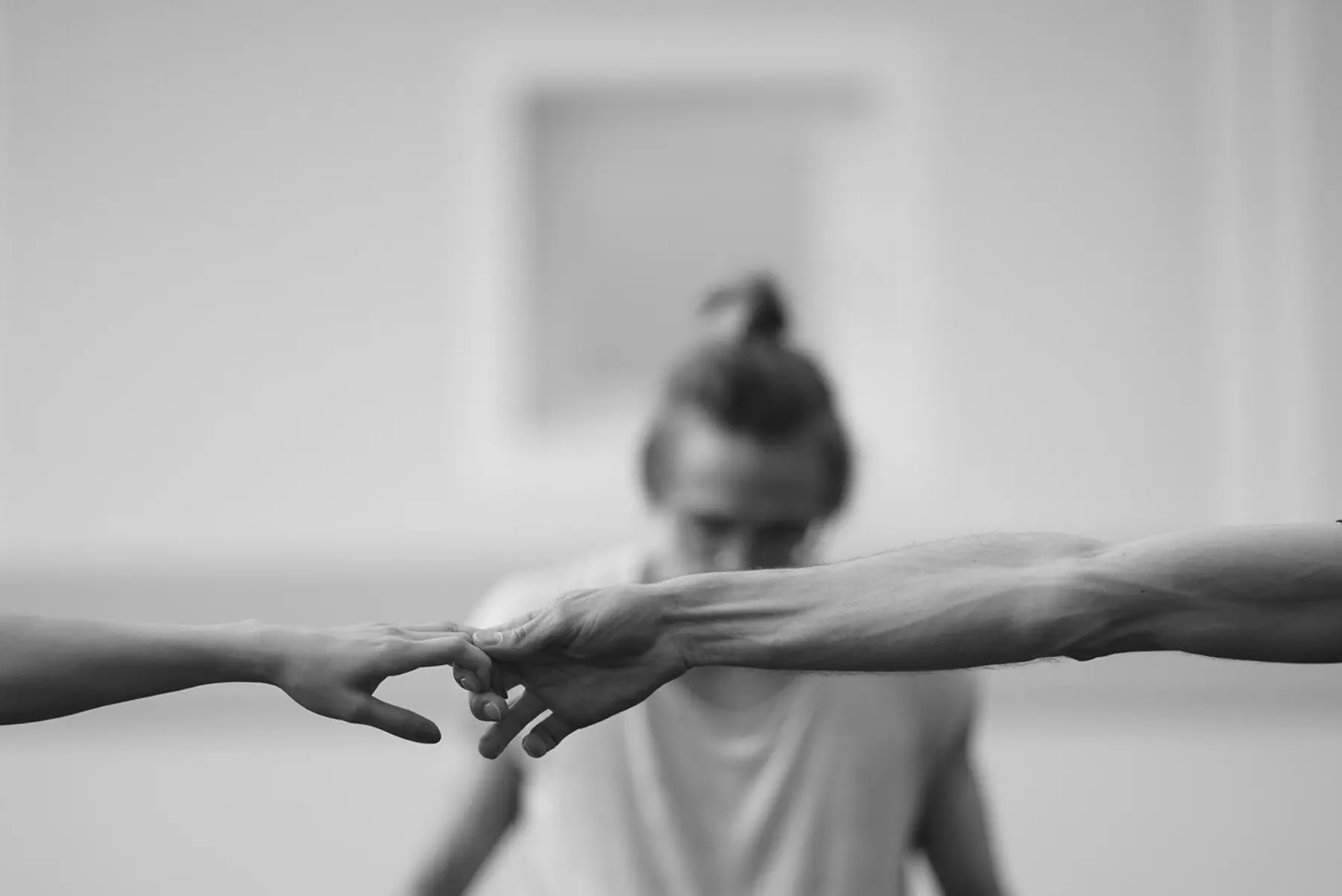 Black and white photo of two hands touching fingertips with a blurred person in the background.