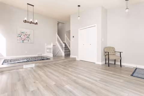 Bright renovated living space with light wood flooring, white walls, modern lighting, and a staircase leading to the upper level.