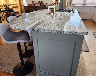 Kitchen island with a grey base, polished granite countertop, and modern bar stools in a bright, open kitchen.