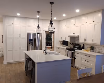 Modern white kitchen with a large island, stainless steel appliances, pendant lighting, and floor-to-ceiling cabinetry.