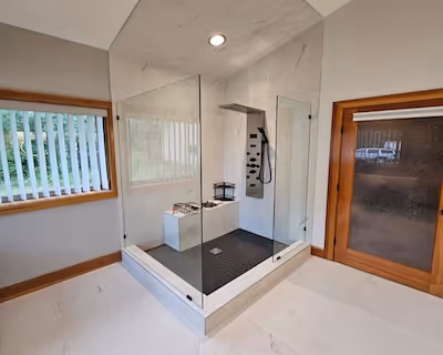 Modern bathroom with a large glass walk-in shower, white tile flooring, and wood-trimmed doors.