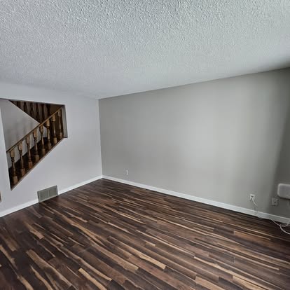 Empty room with dark wood flooring, light gray walls, and an open stairway railing visible through a wall cutout.
