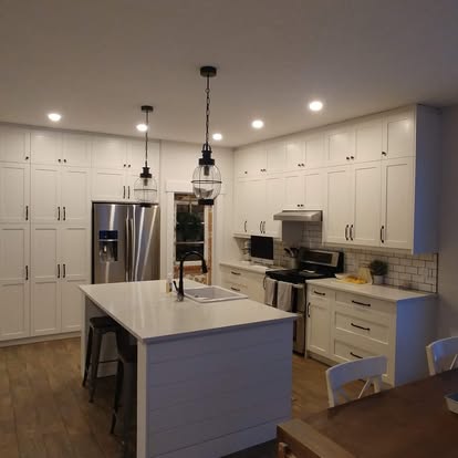Contemporary kitchen with white cabinetry, stainless steel appliances, recessed lighting, and a central island with dark pendant lights.