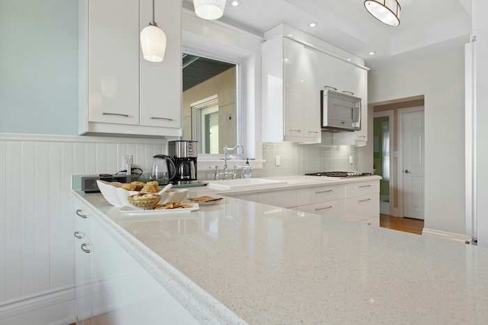 Bright modern kitchen with white cabinetry, sleek quartz countertops, stainless steel appliances, and pendant lighting.