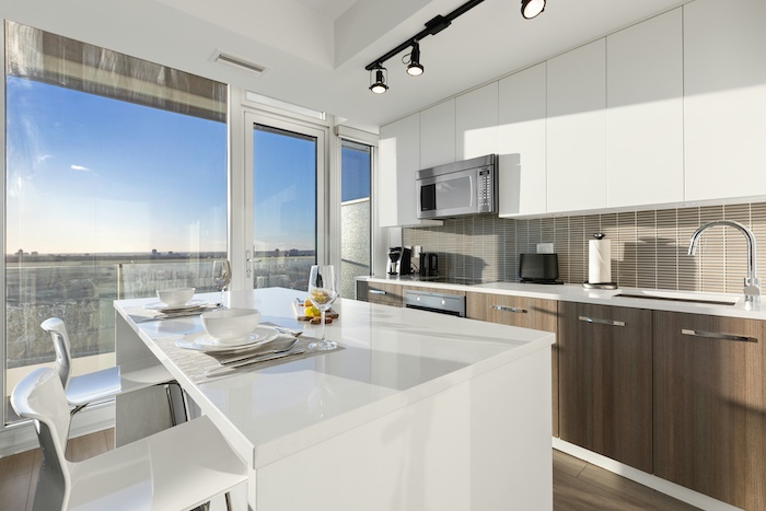 Modern kitchen with bright natural light, white quartz countertops, two-tone cabinetry, stainless steel appliances, and a large window overlooking a clear sky.