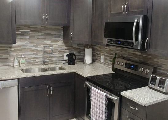 Modern kitchen with dark cabinetry, light countertops, stainless steel appliances, and a gray stone-pattern backsplash.