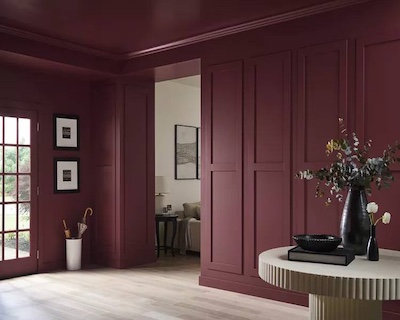 Stylish interior space with deep burgundy paneled walls and ceiling, decorative molding, and a round table with floral arrangements.