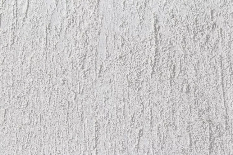 Close-up of a white textured wall surface with vertical, irregular lines and a rough finish.