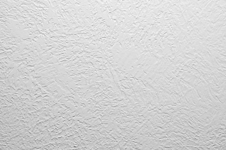 Close-up of a white textured wall surface with vertical, irregular lines and a rough finish.