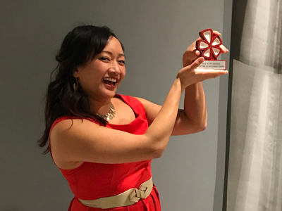 A very happy woman holding up a small awards statue