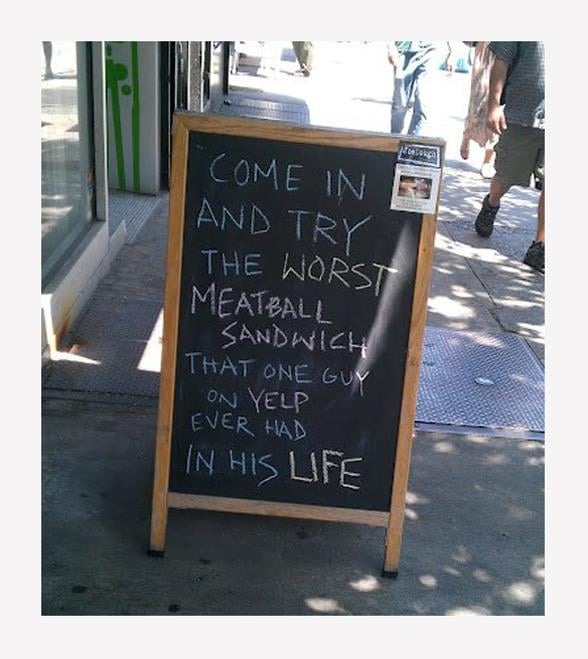 A chalkboard on a sidewalk that says "Come in and try the worst meatball sandwich that one guy on Yelp ever had in his life"