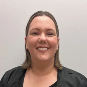 Smiling woman with shoulder-length light brown hair wearing a black top against a plain light gray background.