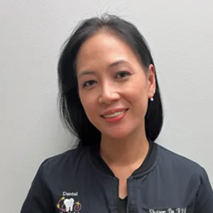 Smiling female dental hygienist with black hair wearing a navy dental jacket.