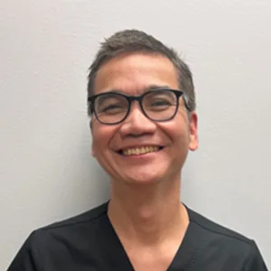 Smiling man with glasses and short black hair wearing a black shirt against a plain light gray background.