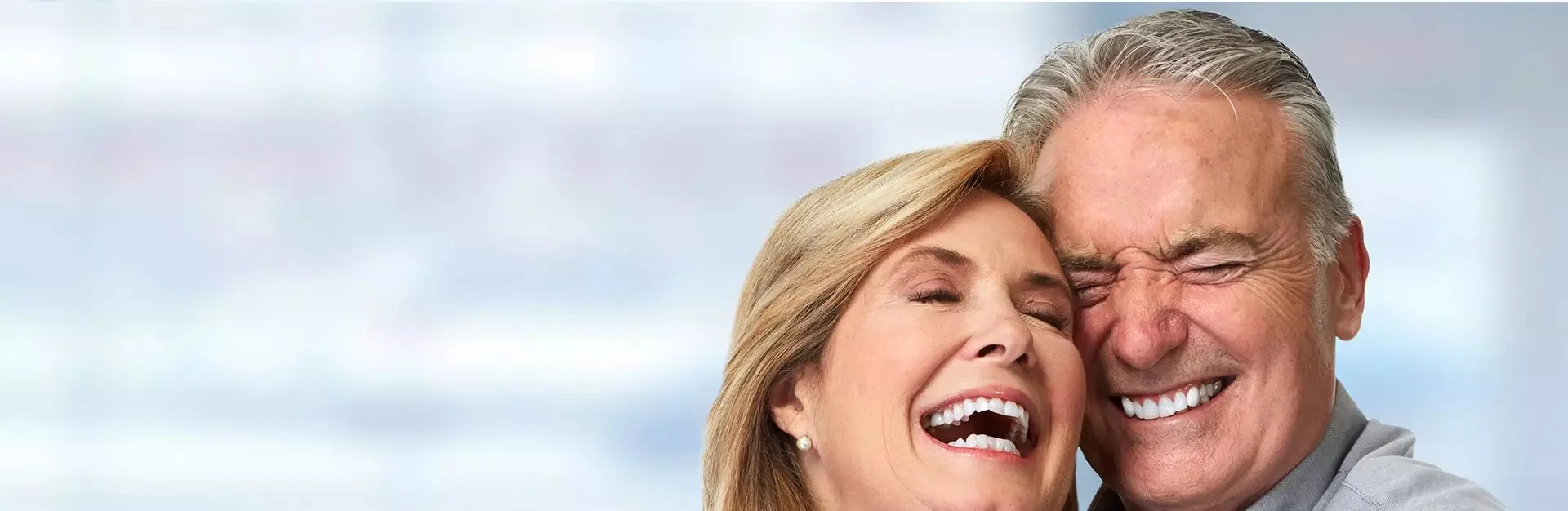 Smiling elderly couple with eyes closed, embracing and laughing together.