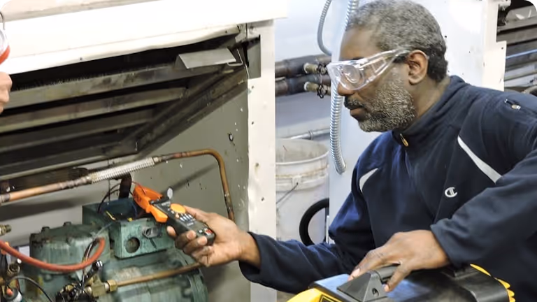 Technician wearing safety goggles inspecting machinery with a handheld device.