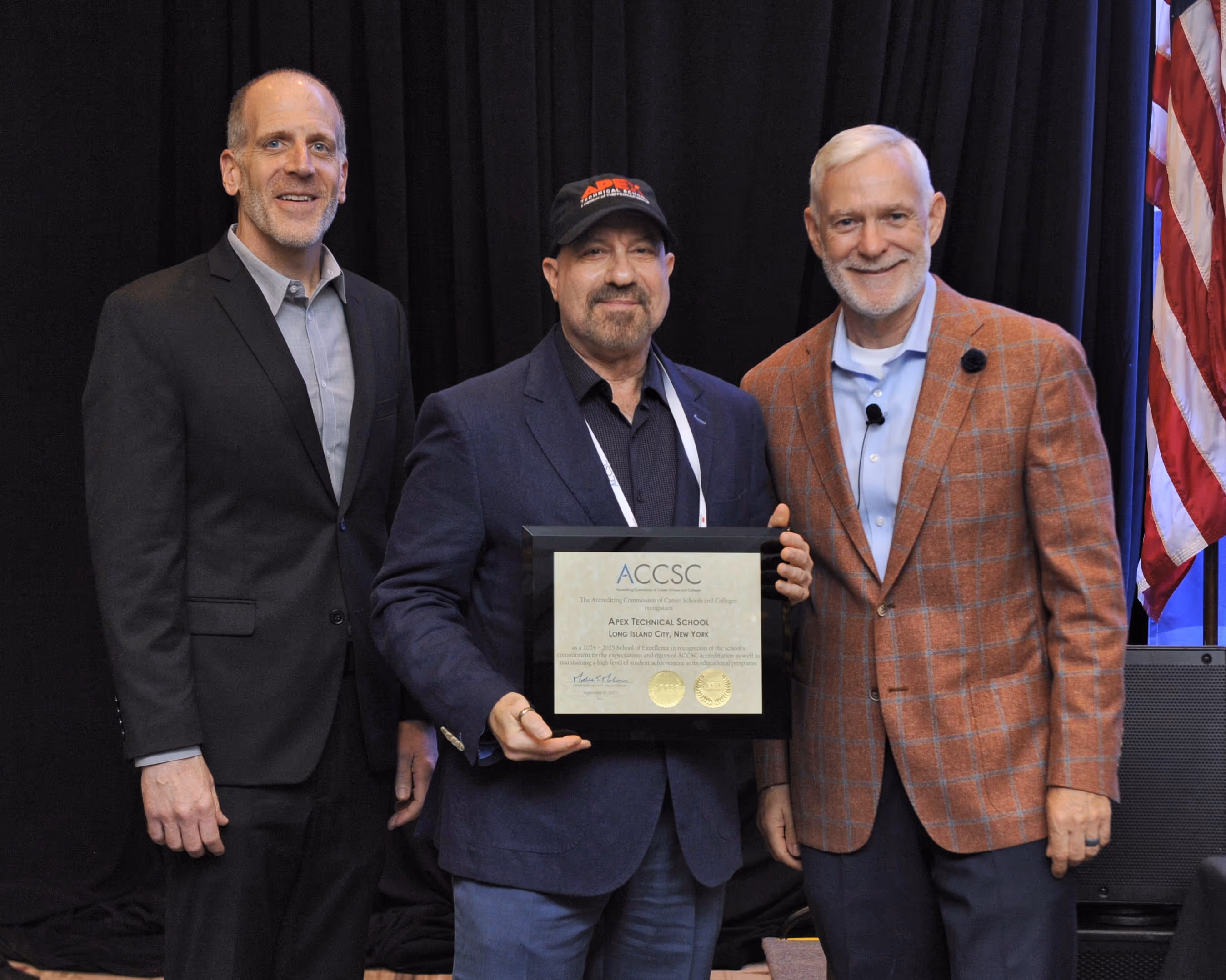 Three men standing together, with the center man holding an ACCSC award certificate for Apex Technical School.