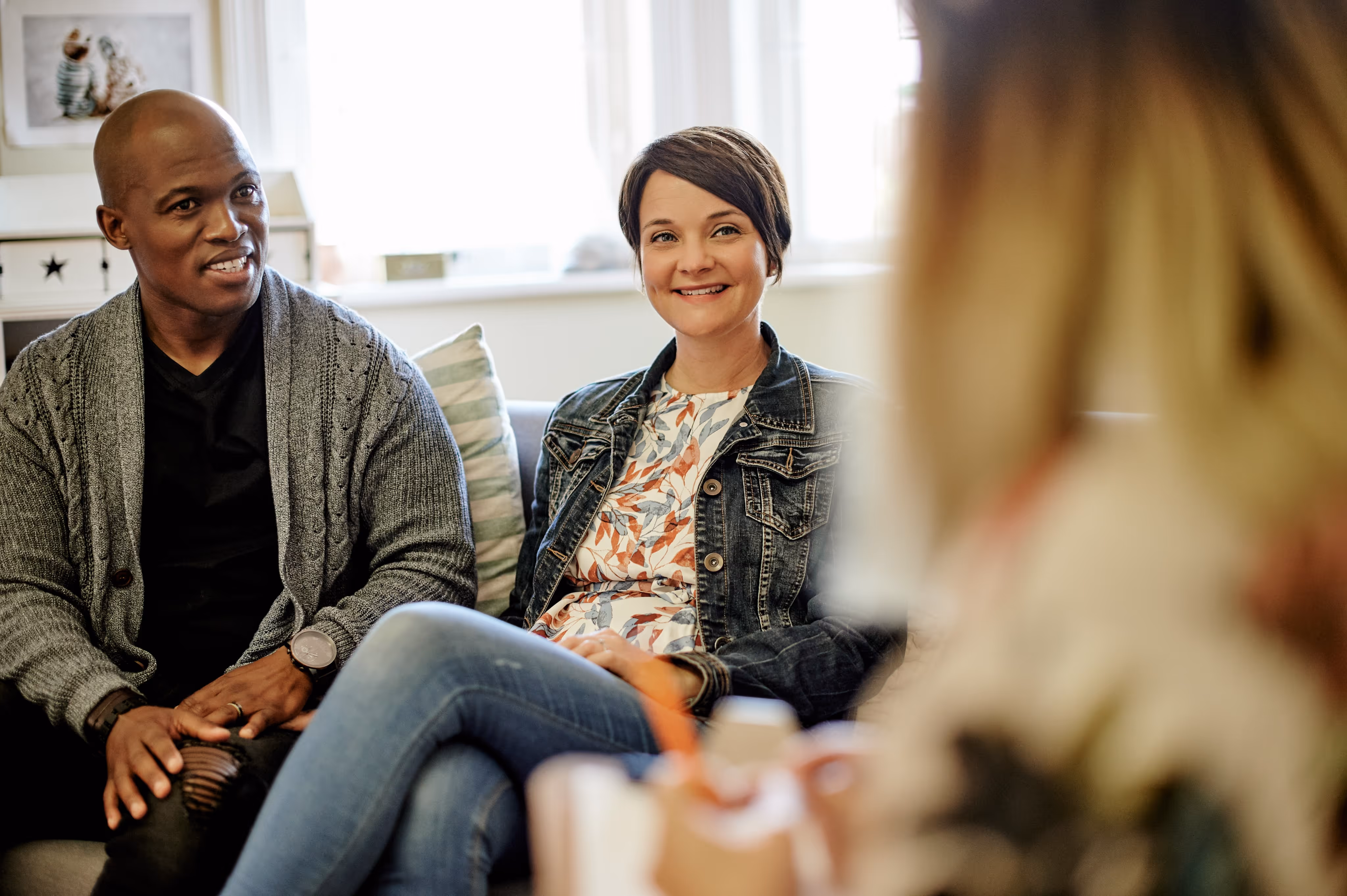 Couple sitting on a couch engaged in a conversation with another person.