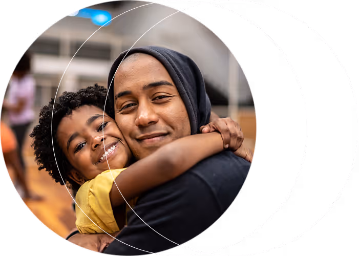 Smiling young boy in yellow shirt hugging a man in a dark hoodie inside a gym.