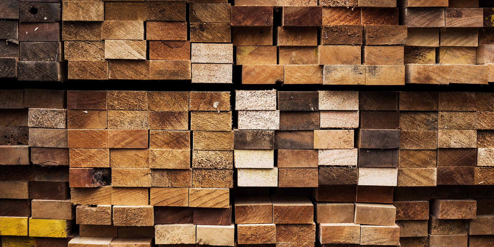 Gestapelte Holzbohlen verschiedener Brauntöne in einem Holzlager.