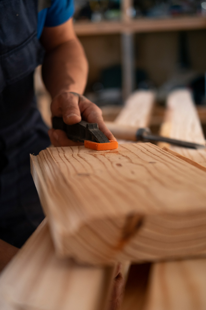 Nahaufnahme eines Handwerkers, der mit einem Meißel an einem Holzbrett arbeitet.