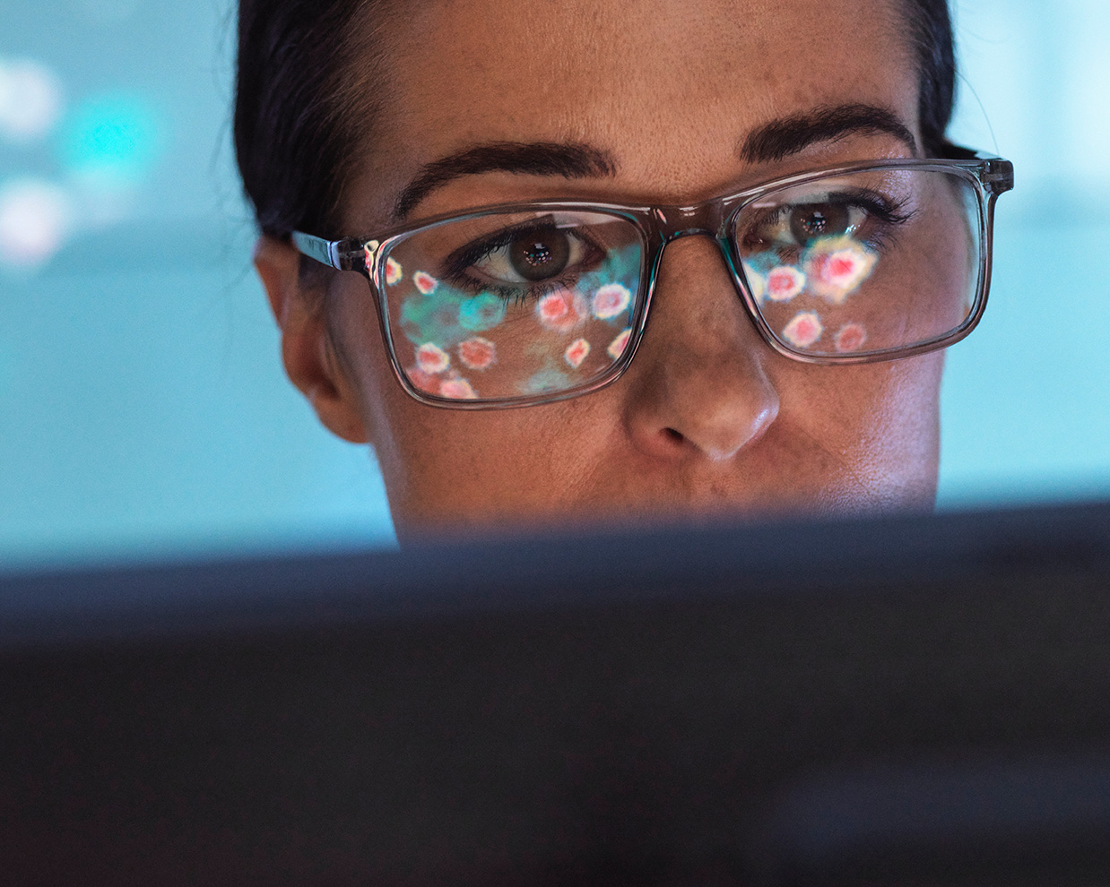 Close-up of a woman wearing glasses looking at a screen with digital data reflected in the lenses.