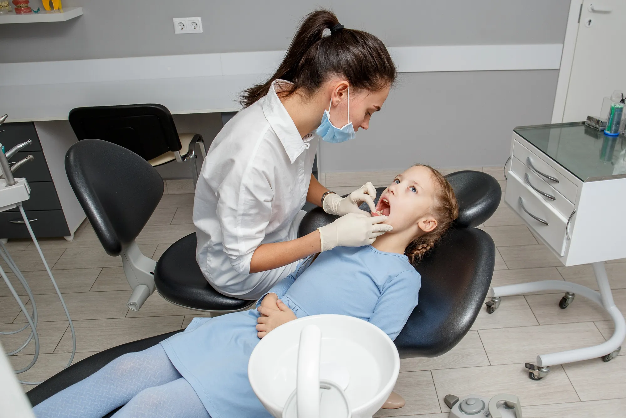 Kid getting her teeth checked by a reading dentists