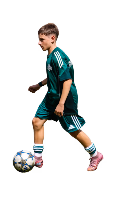 Young boy in green soccer uniform dribbling a soccer ball with pink cleats.