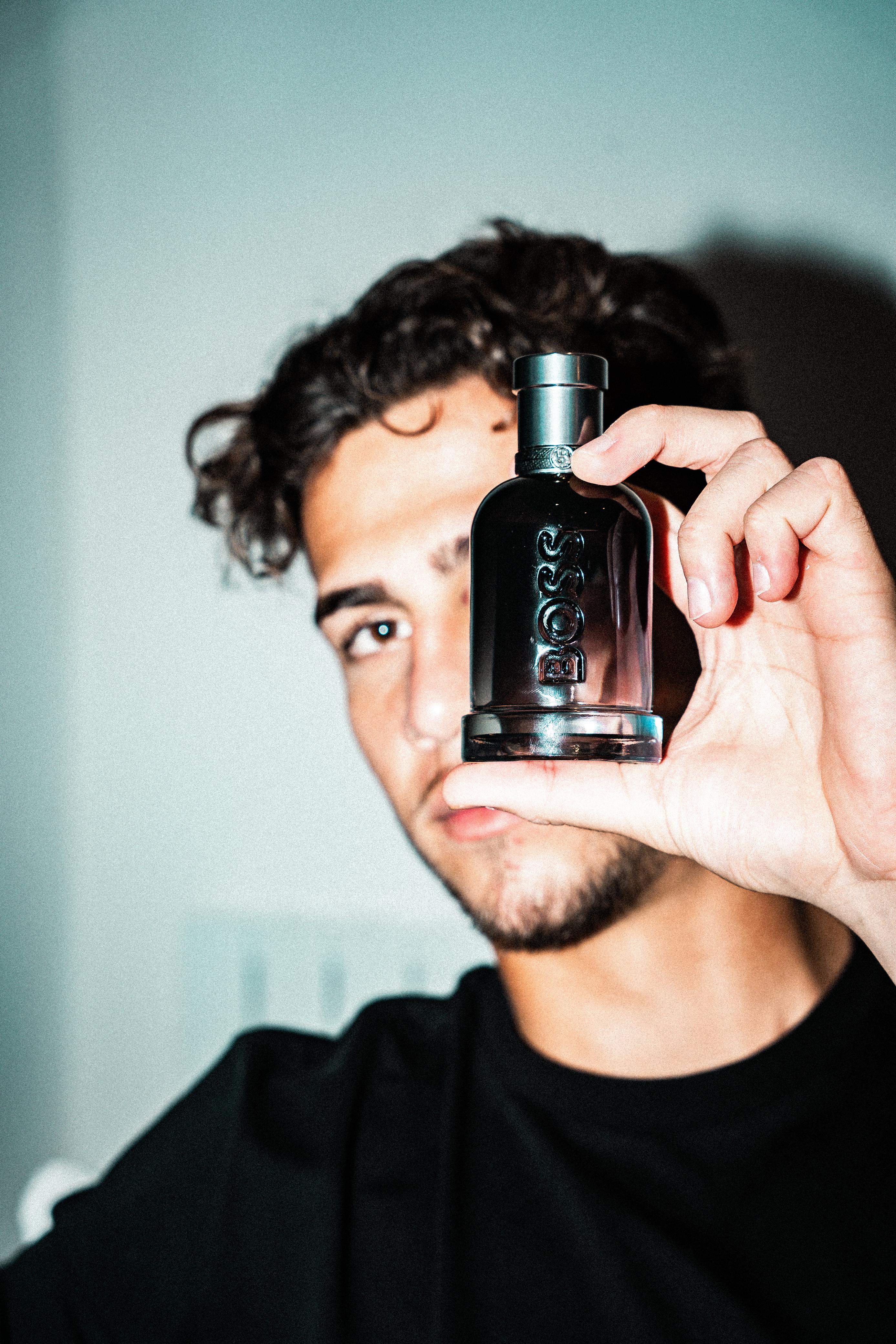 Man holding a black Hugo Boss cologne bottle close to his face.
