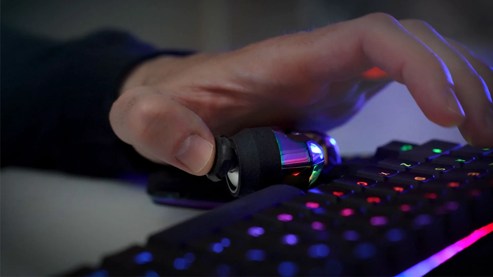Close-up of a hand gripping the Mimic joystick controller next to a colorful backlit gaming keyboard.