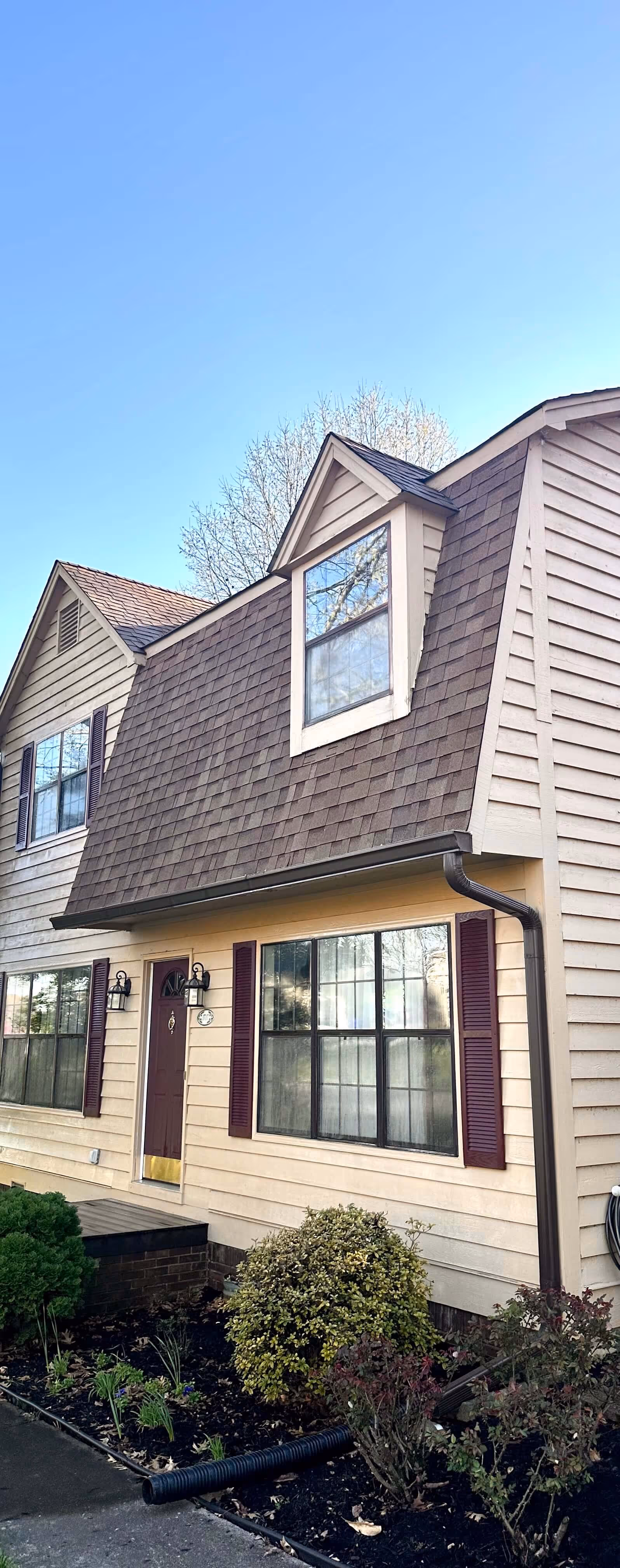 Two-story beige house with brown shingle roof, and large front windows