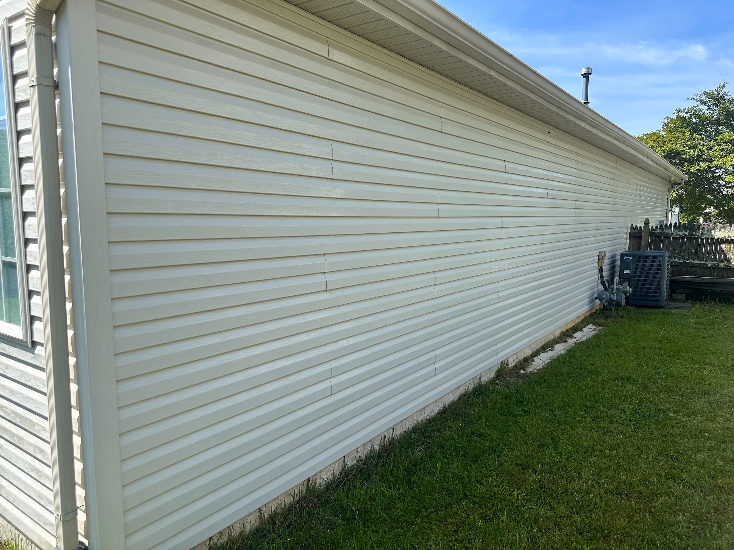 Vinyl siding on the side of a house completely cleaned after a professional soft wash treatment.
