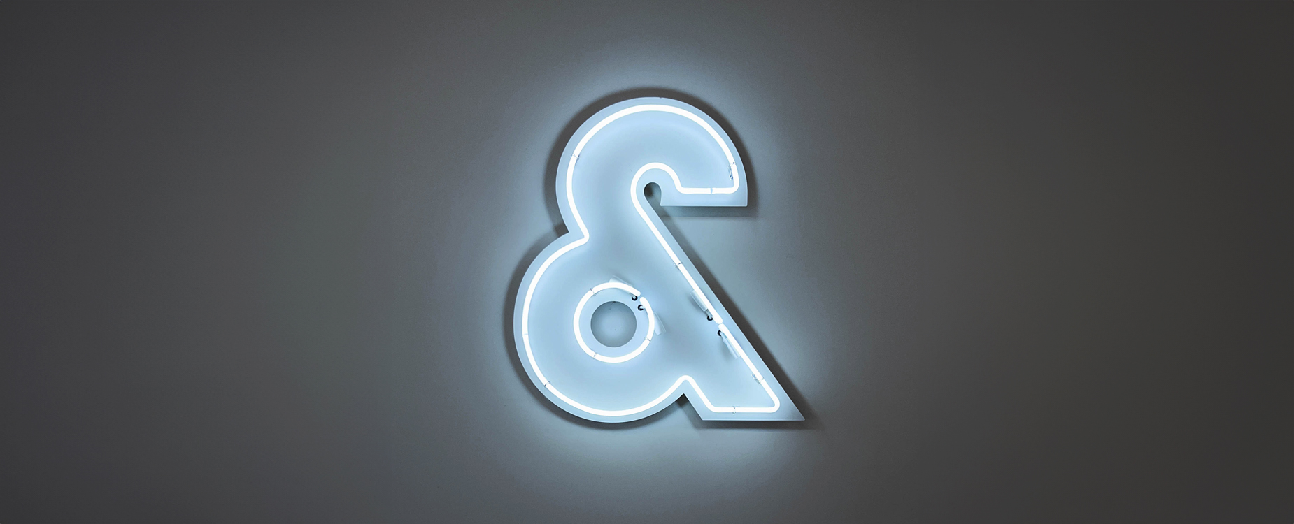 Glowing white neon ampersand symbol on a dark gray wall.