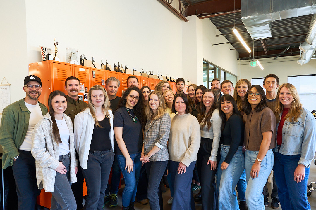 Group of diverse coworkers smiling in an office with orange lockers and awards behind them.
