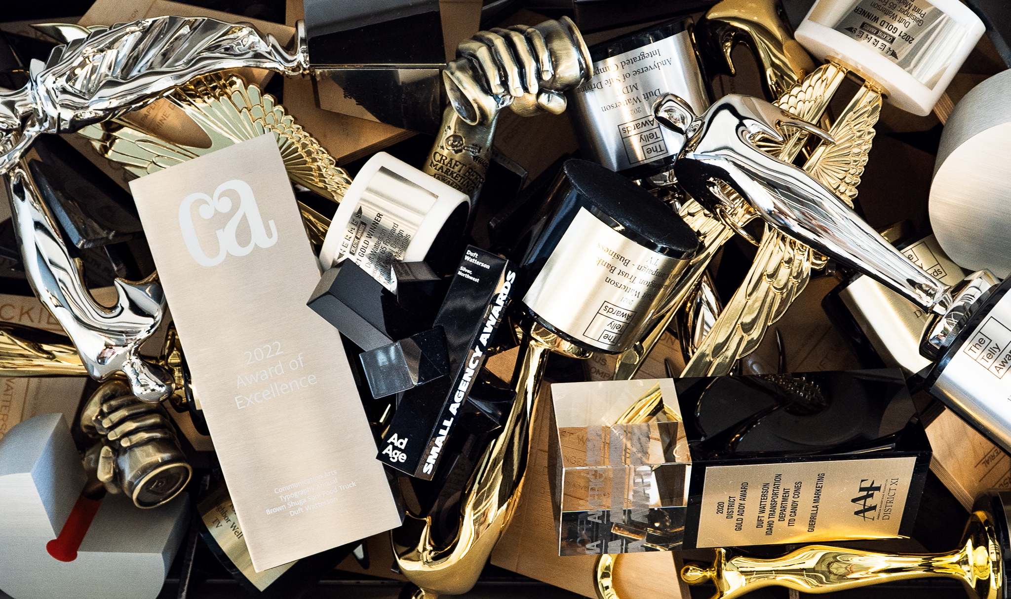 Close-up of multiple gold and silver trophies and awards piled together for marketing and advertising achievements.