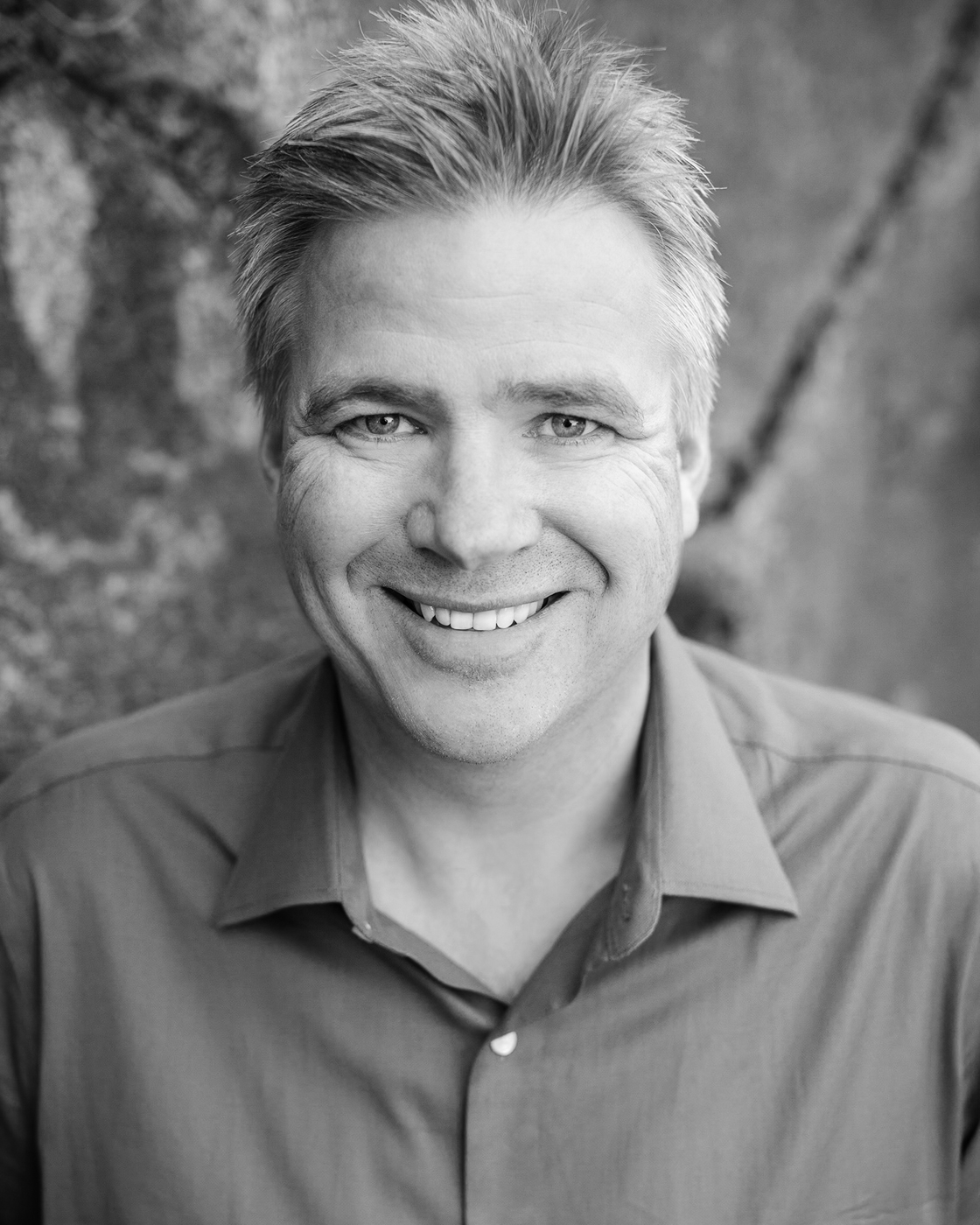 Smiling middle-aged man with spiky hair wearing a collared shirt in a black-and-white photo.
