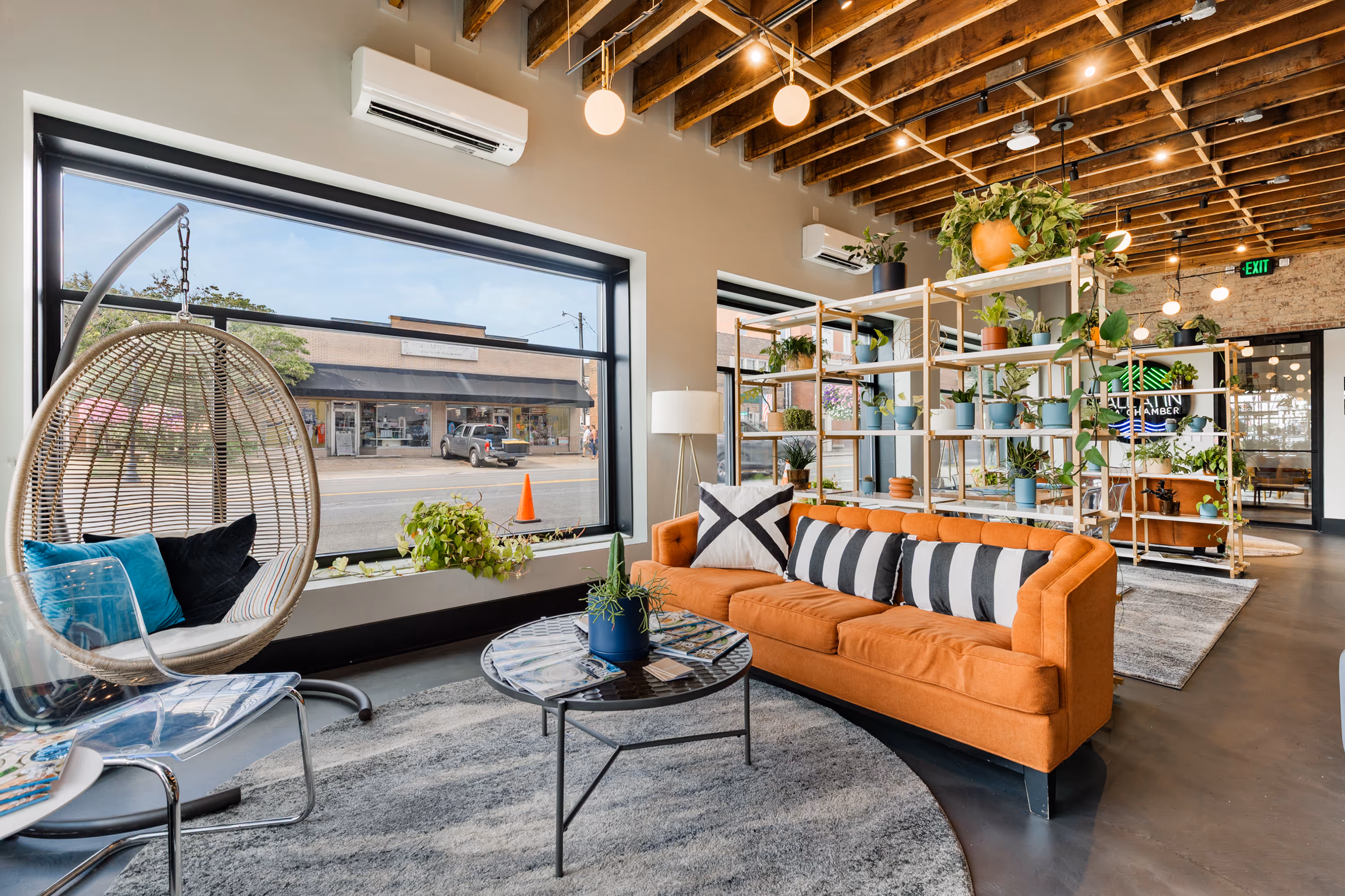 Common space in Station Gallatin with a bright orange couch and plants with a window facing downtown Gallatin.