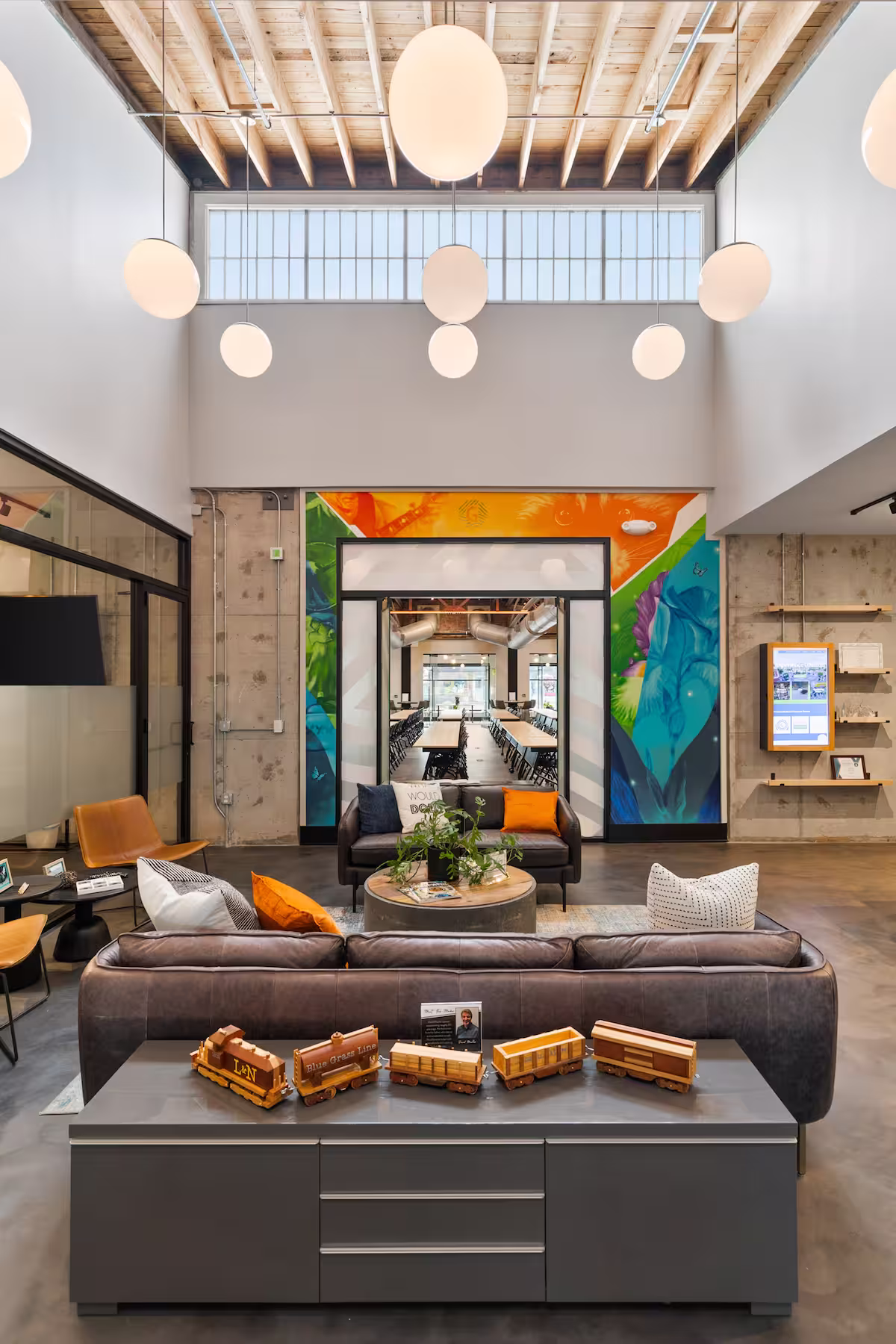 Hallway area of office complex with hanging plants above and high chairs seated at a bar near the shared kitchen area