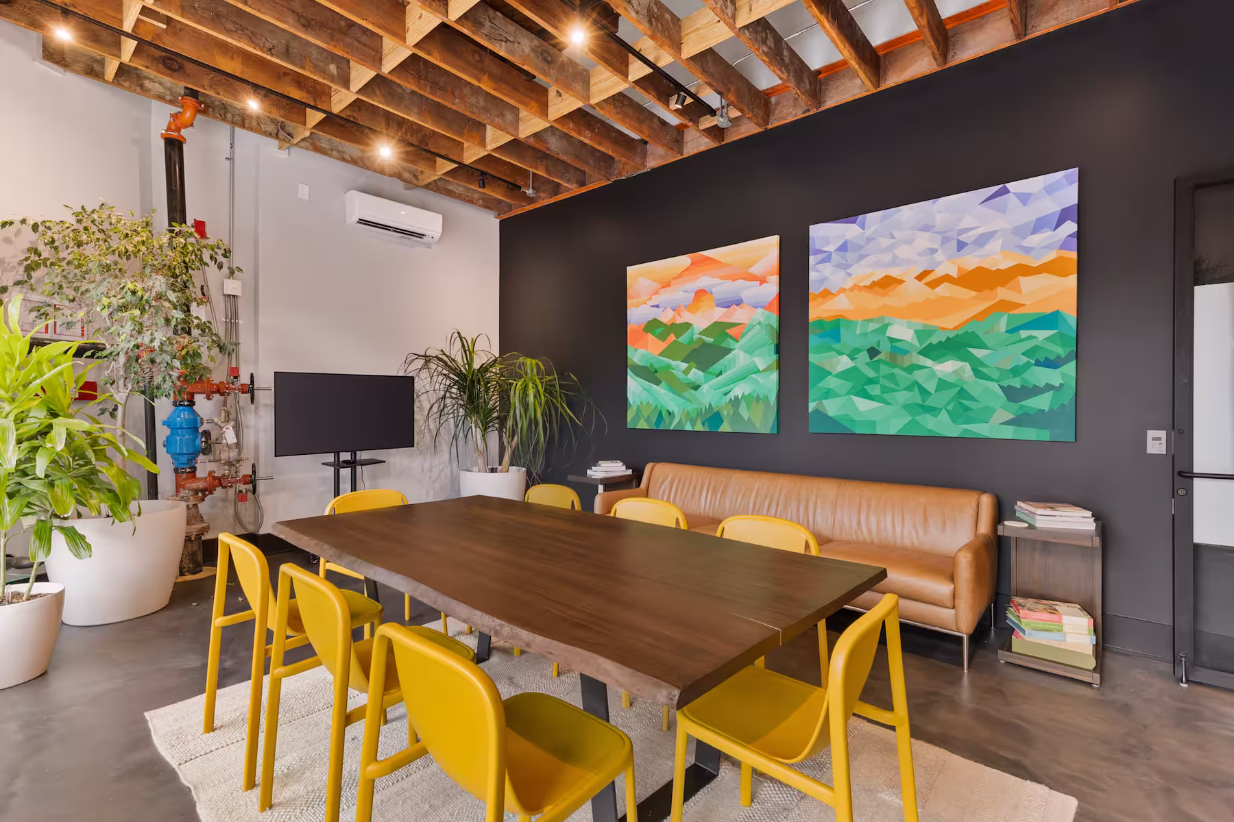 Meeting room with large wall art, a big wooden table, colorful chairs, and television on the back wall