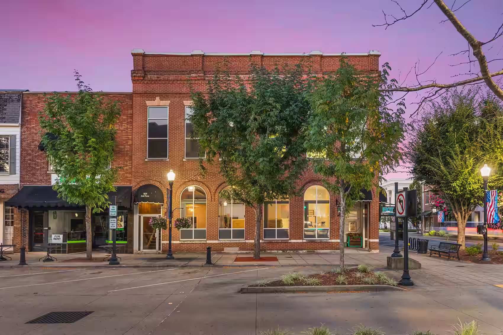 Brick office complex at the intersection between two roads with trees in front of it at twilight