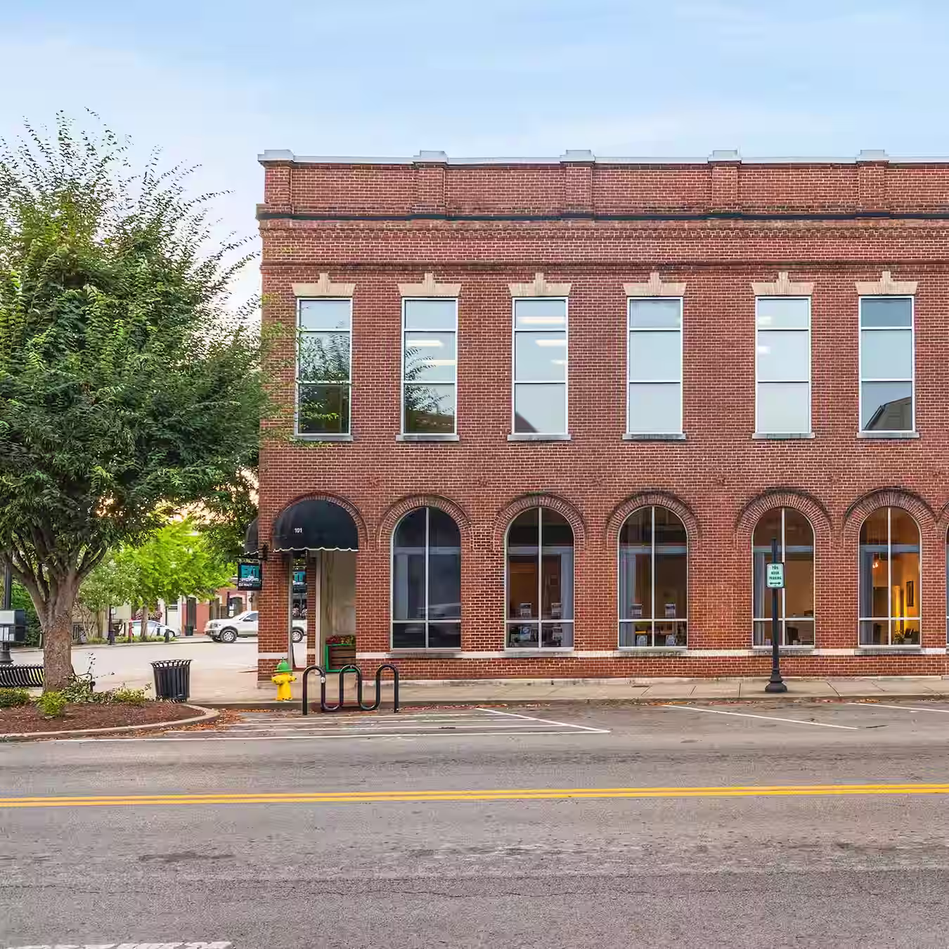 Brick office complex at the intersection between two roads with trees in front of it.