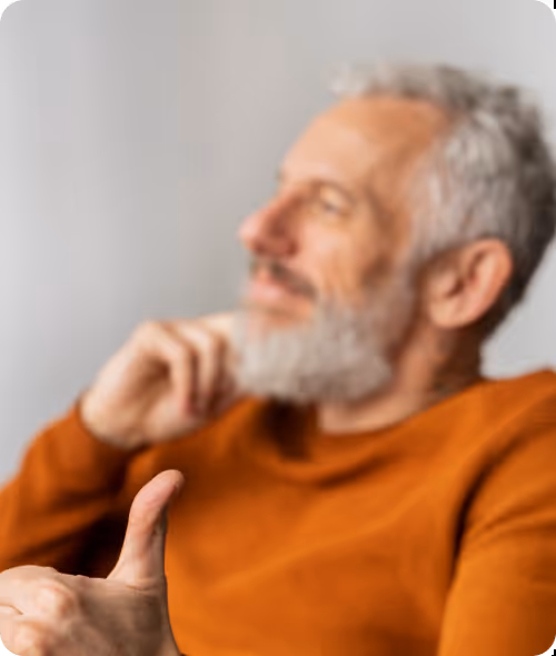 Hombre mayor con barba blanca y suéter naranja mostrando un pulgar hacia arriba y sonriendo.