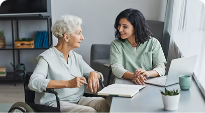 Mujer joven profesional hablando con una mujer mayor en silla de ruedas en una oficina.