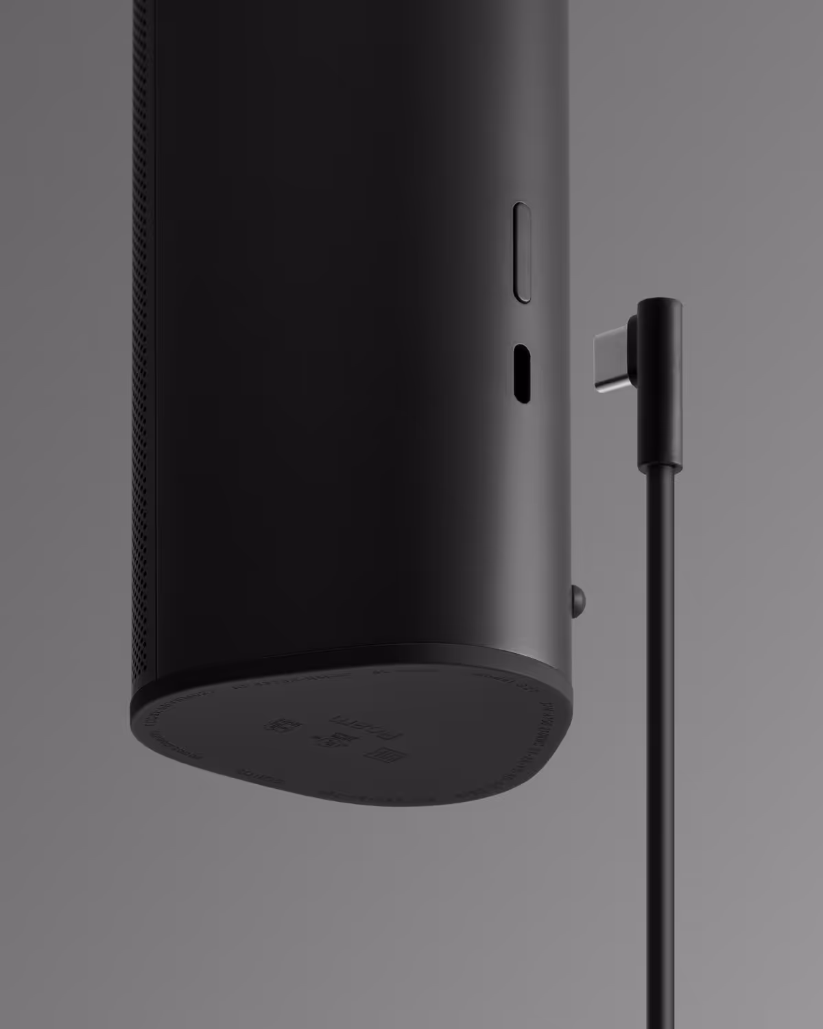Black cylindrical speaker positioned upside down next to a matching angled USB-C charging cable.