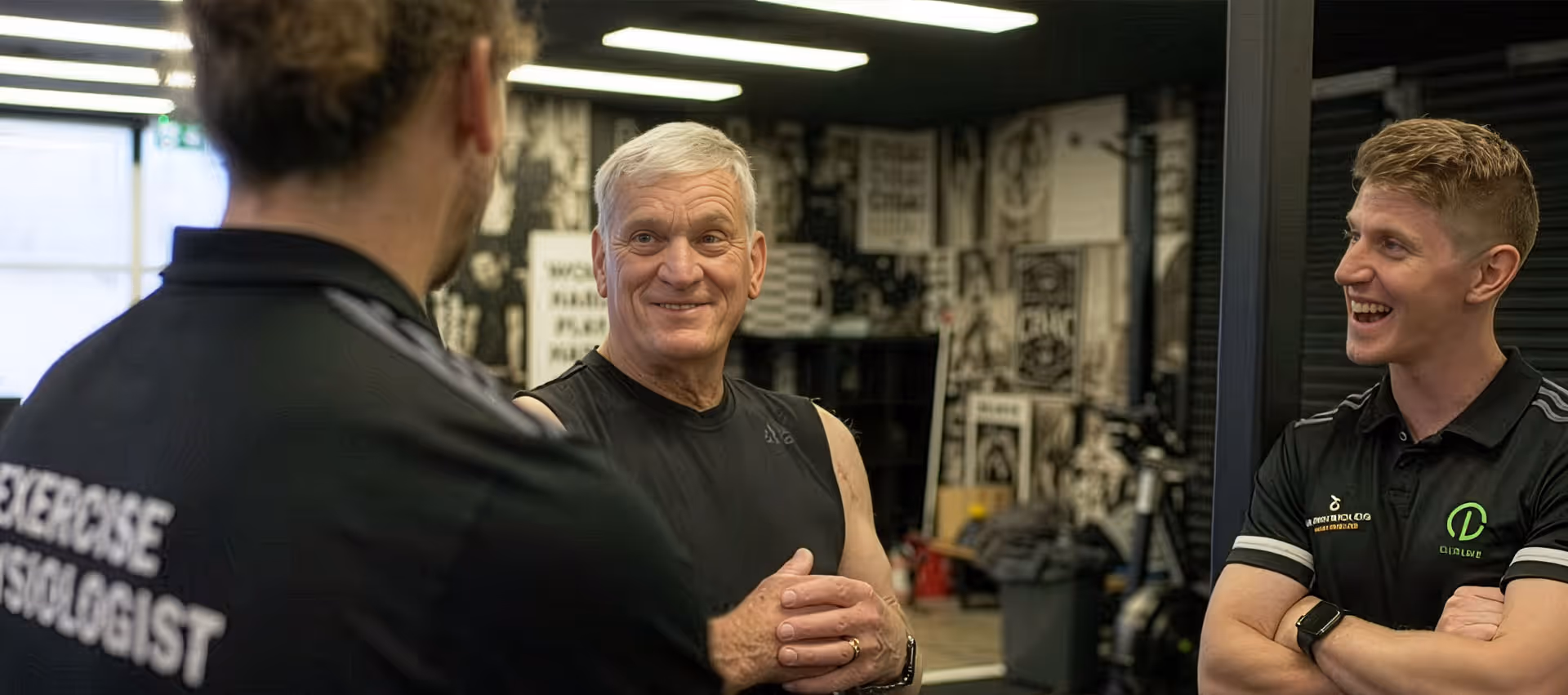 Three men in a gym, including two exercise physiologists talking and smiling with an older man in workout attire.