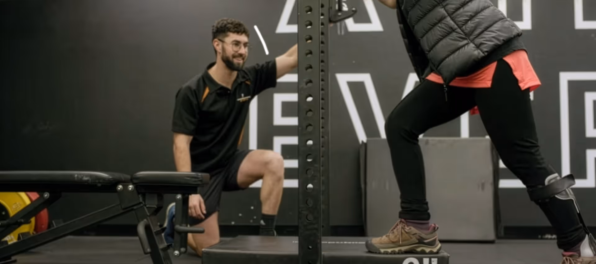 exercise physiologists kneeling on one knee and providing guidance to a person exercising stepping on a platform.