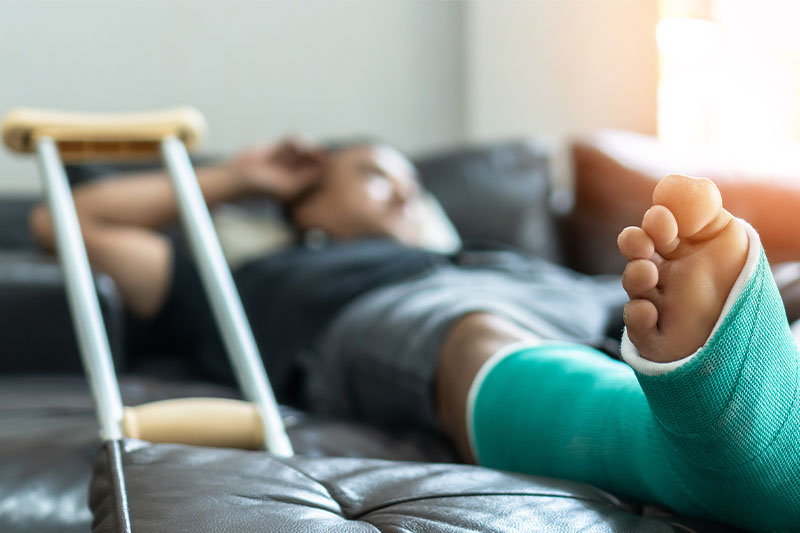 Person lying on a couch with a green cast on their leg and crutches nearby.